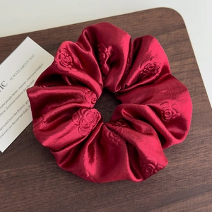 Primo piano dell'elastico scrunchie in raso rosso scuro con motivo floreale di rose in rilievo