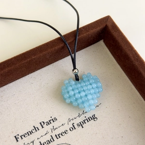 Vue détaillée du pendentif cœur en perles bleu clair sur un cordon noir réglable