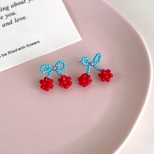 Sweet blue beaded bow and red cherry drop earrings on a pink aesthetic tray