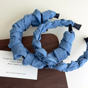 Détails des serre-têtes en tissu bleu denim froncé et tressé sur un support bois