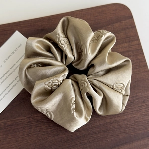 Dettaglio dell'elastico in raso oro champagne con motivo jacquard a rose su legno scuro