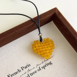 Vue détaillée du pendentif cœur en perles jaunes sur un collier en cordon noir