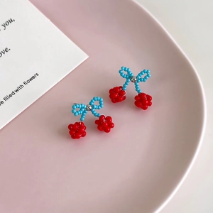 Detailed macro shot of red and blue beaded cherry earrings on a decorative pink plate