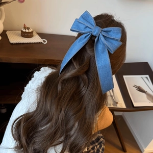 Blue denim bow hair clip with yellow stitching detail shown on long curly hair