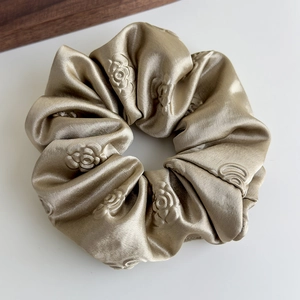 Dettaglio dello scrunchie in raso champagne con rose in rilievo 3D e consistenza setosa
