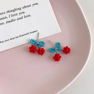 Handmade cherry beaded stud earrings with blue bow on pink ceramic display tray