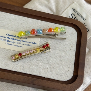 Detailed macro shot of two sparkling rainbow crystal hair clips on a wooden tray