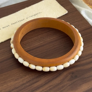 Detail view of a bohemian wood bangle and white beaded bracelet set on a walnut tray