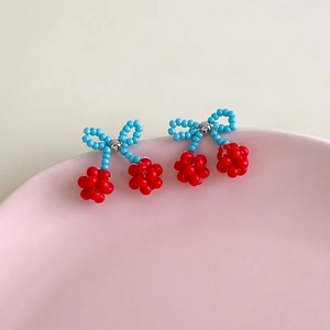 Macro detail of handmade beaded cherry earrings with blue bow and red cherry pendants