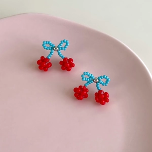 Close-up of handmade beaded cherry earrings with blue bows on a pink ceramic plate