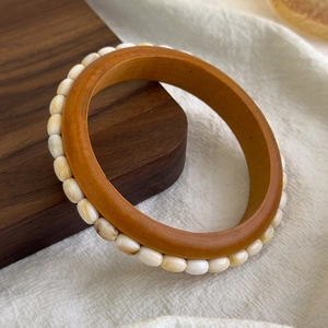 Detailed view of the wooden bangle featuring inlaid cream-colored oval beads and studs