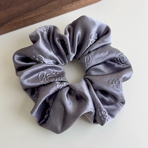 Dettaglio dello scrunchie in raso argento con rose goffrate 3D e lucentezza setosa