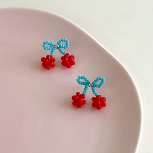 Detailed shot of handmade beaded cherry earrings with blue bows on a pink ceramic tray