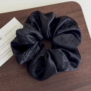 Dettaglio di scrunchie in raso nero con motivi a rosa goffrati su base in legno