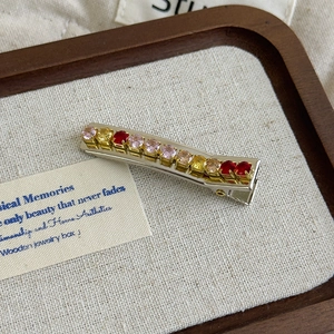 Close-up of a silver duckbill hair clip with gradient pink and yellow rhinestones
