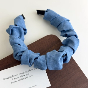 Détail d'un serre-tête bleu style denim froissé montrant la texture sur bois naturel