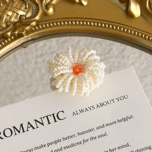 Detail of a handmade white beaded flower charm with an orange center for DIY shoe clogs
