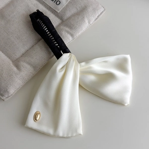 Detail view of cream satin bow banana clip with elegant golden embossed metallic emblem
