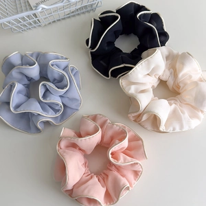 Detailed view of ruffled fabric hair scrunchies in pastel blue, black, beige and pink