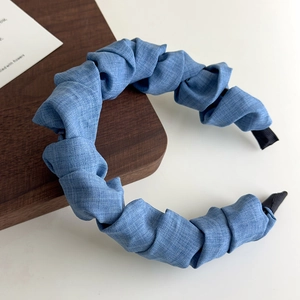 Détail du bandeau en jean bleu plissé avec embouts noirs antidérapants sur fond en bois