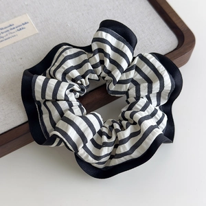 Close-up of black and white striped scrunchie with ruffled edges on a wooden tray