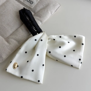 Detailed close-up of a white satin polka dot bow clip with a golden metallic logo plate
