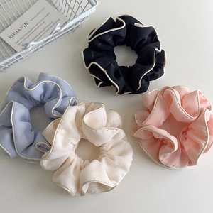 Detail of four large pleated scrunchies in pastel colors with contrast piping