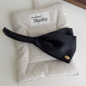 Detail of elegant black satin bow hair clip with a gold logo on a linen pouch