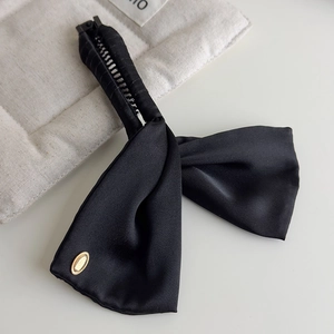 Detail of black satin bow banana clip with elegant gold oval metal tag on white quilted background
