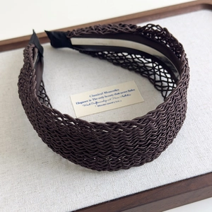 Detailed close-up of dark brown bohemian hollow-out woven headband on a wooden tray