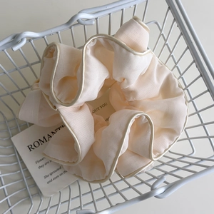 Detail of cream pleated scrunchie with champagne gold piping in a minimalist metal basket