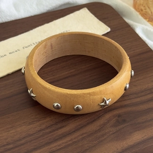Detailed view of wooden bangle with silver star studs and rivets on rustic display