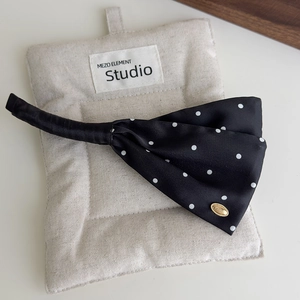 Detailed view of black satin polka dot bow hair clip with gold metal emblem on fabric