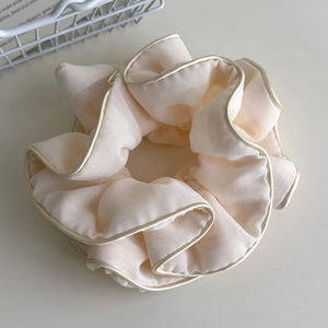 Detailed view of beige pleated fabric scrunchie with elegant satin trim and soft chiffon texture