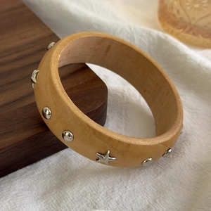 Detail of wooden bangle with silver star and rivet accents on rustic tray background