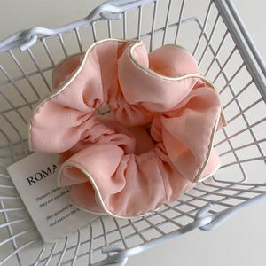 Close-up of pink fabric scrunchie with white piping edge inside a white iron basket