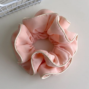 Close-up of pink pleated fabric scrunchie with cream piping trim and chiffon texture