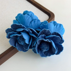 Close-up of vintage denim camellia flower hair clip with frayed edges on a wooden base