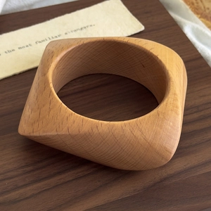 Detail view of a square wooden bangle showing natural wood grain texture on a rustic tray