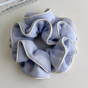 Top view of a light blue organza scrunchie with cream piping on a minimalist grey desk