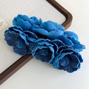 Detailed view of blue denim camellia flower hair clip on a display board with wood frame