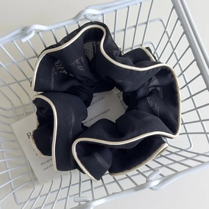 Detail of a black pleated hair scrunchie with cream borders inside a white wire basket