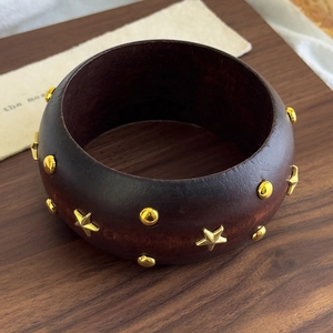 Close-up of a wide dark wood bangle featuring gold star and stud rivets in retro style