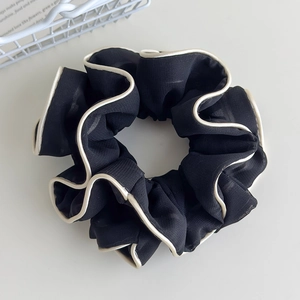 Detail of black chiffon scrunchie with white piped edges and pleated fabric texture