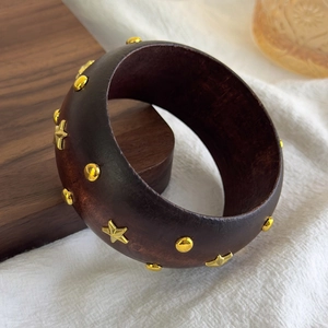 Close-up of geometric wooden bangle with gold star studs and metal rivet details