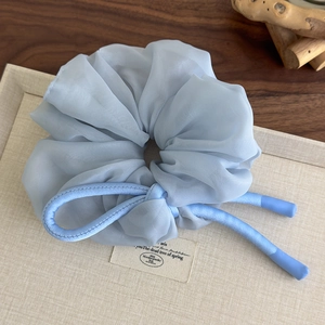 Close-up of light blue chiffon scrunchie with layered organza texture and sleek decorative cord