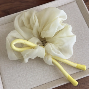 Macro detail of creamy chiffon scrunchie with a bright yellow satin bow on a display tray