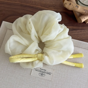 Close-up of cream organza scrunchie featuring a contrasting yellow satin ribbon bow detail