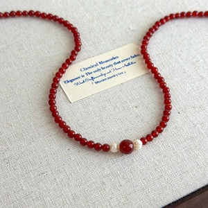 Detail of red agate beaded necklace with white pearls on a soft beige textured background