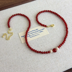 Detailed view of red agate beaded necklace with white pearls and gold lobster clasp